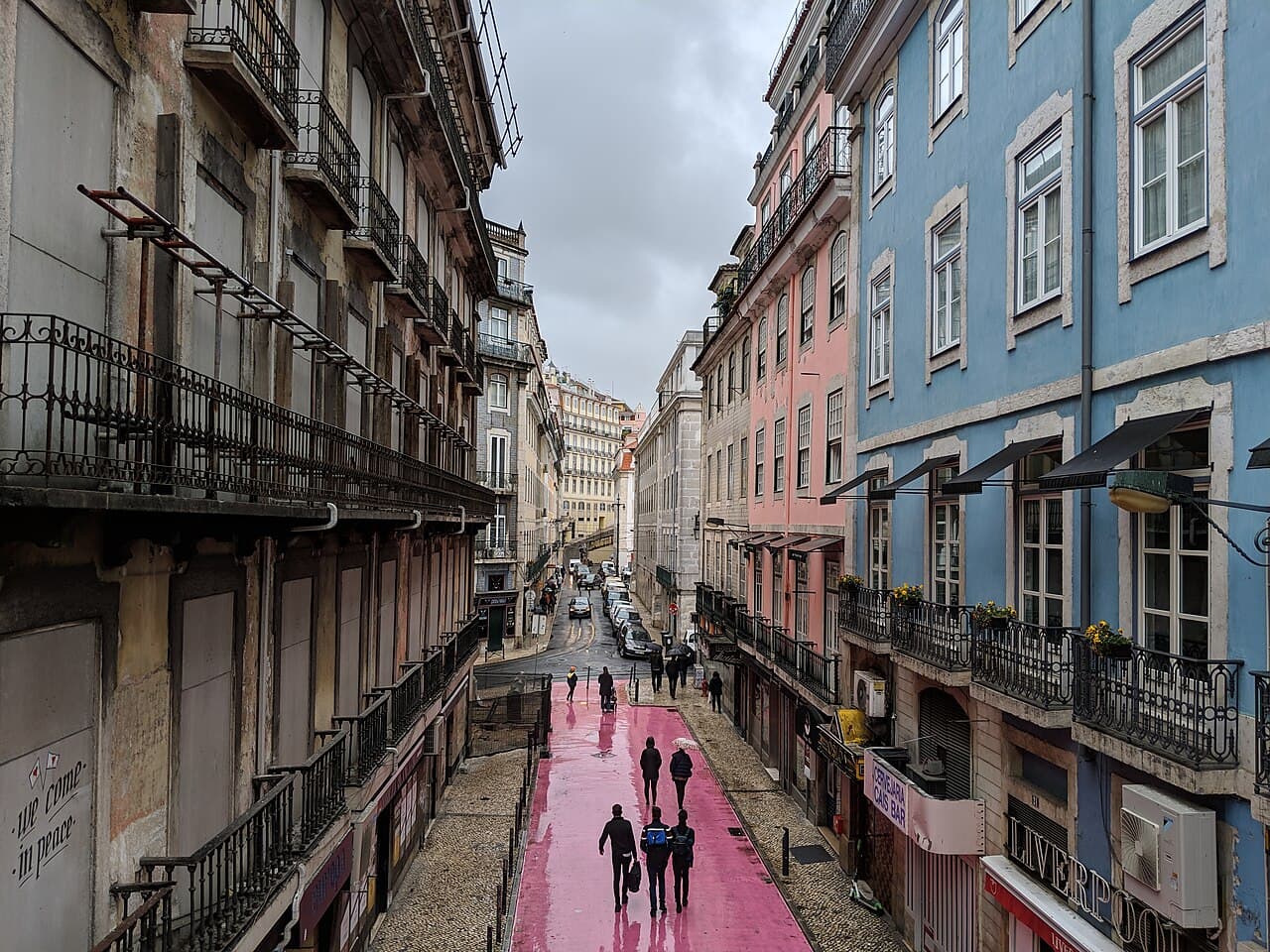 The pink-painted Rua Nova do Carvalho crowded at night under umbrellas