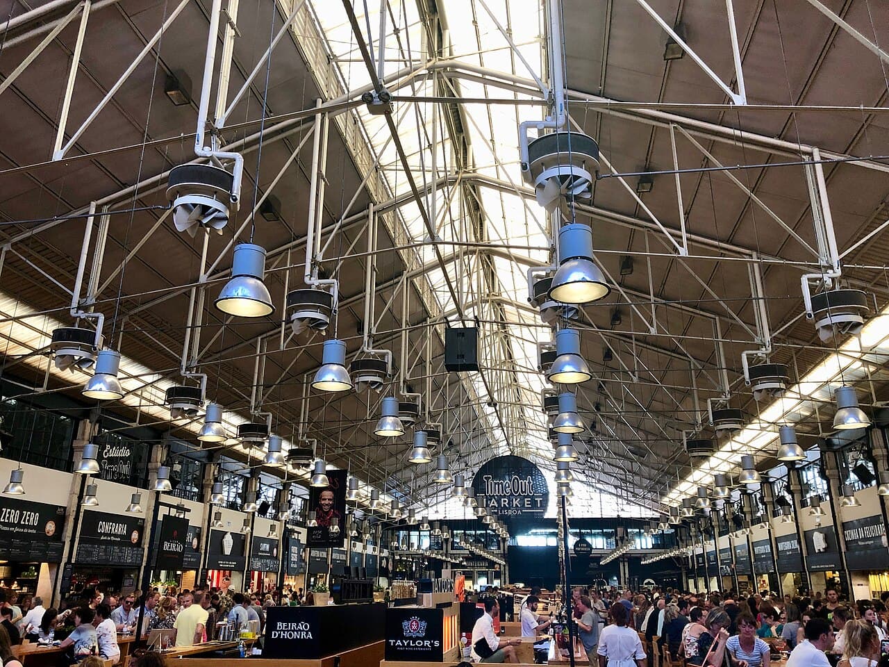 Communal tables and food counters under the iron roof of Time Out Market