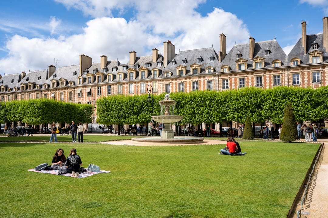People relaxing on the lawn of the arcaded Place des Vosges under a blue sky